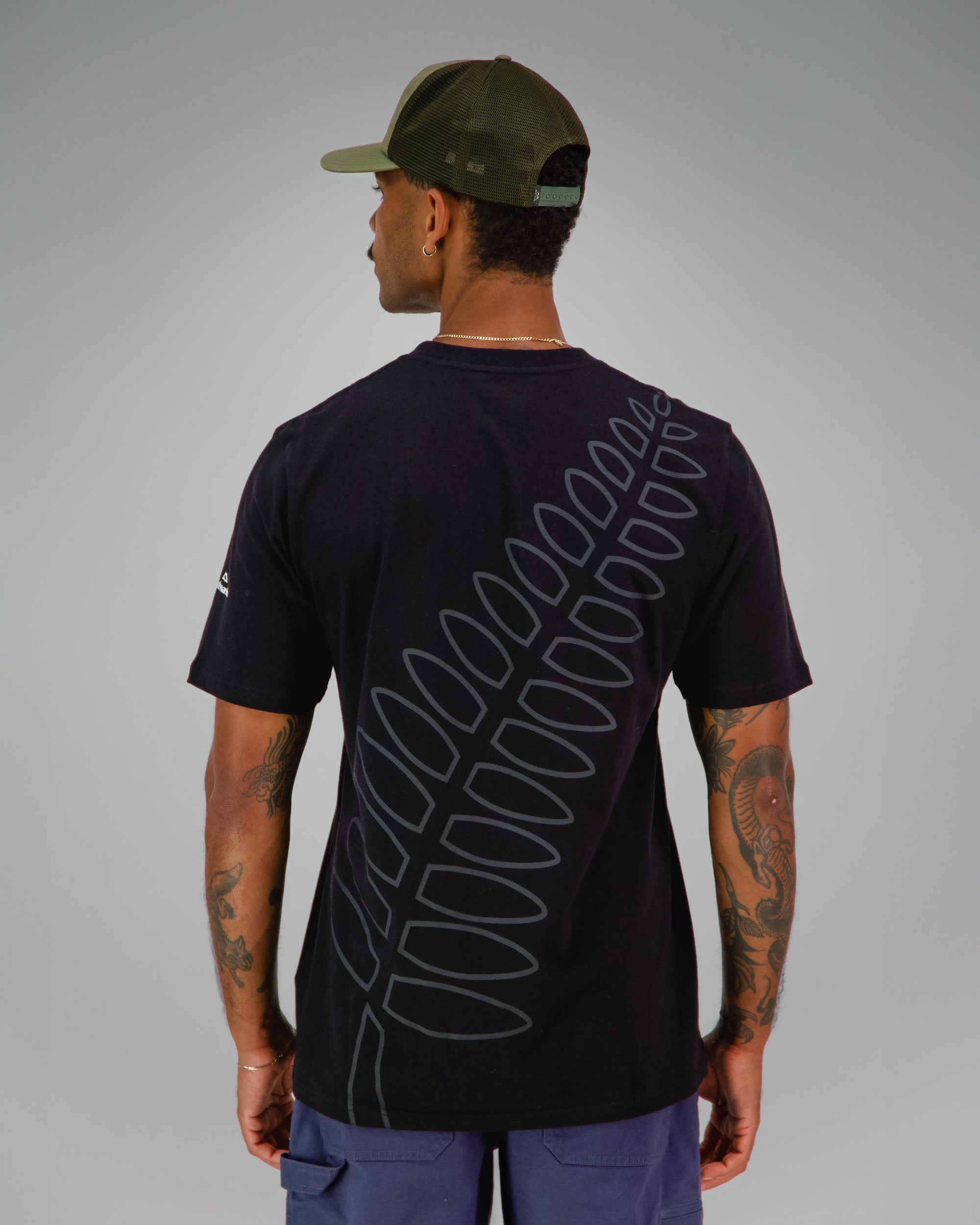 Man wearing a black t-shirt with NZ Team Fern print covering the back in dark grey.