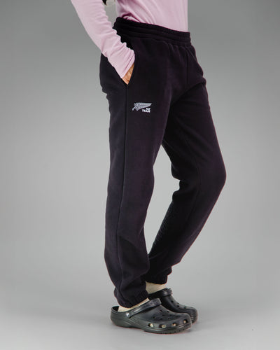 Person wearing black jogger pants with a NZ team logo
