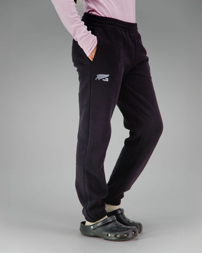 Person wearing black jogger pants with a NZ team logo